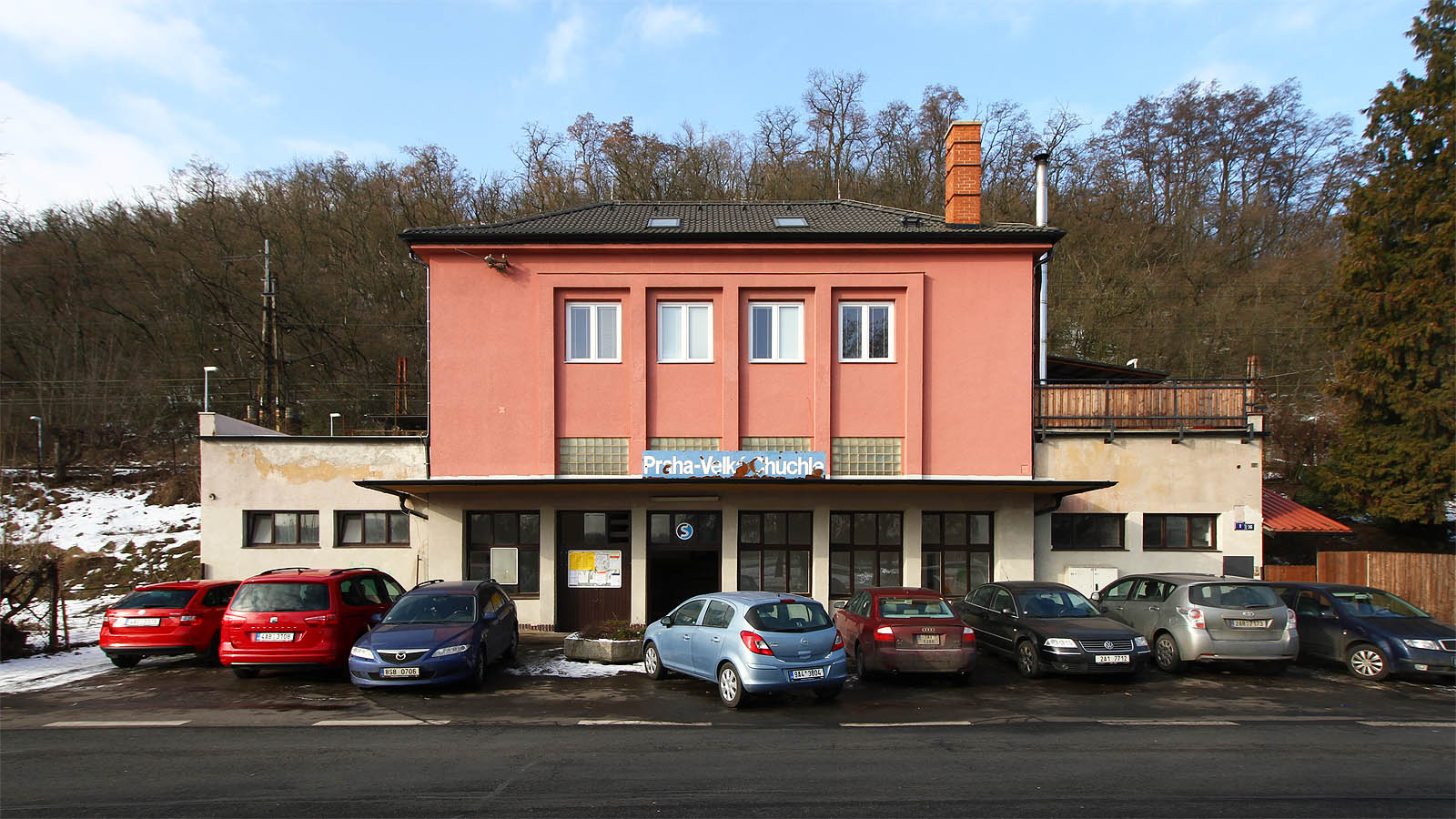 Pohled na budovu zastávky z Radotínské ulice. Praha-Velká Chuchle působí spíš jako stanice, protože disponuje čtveřicí kolejí, ostrovními nástupišti a velkolepě pojatými prostory pro cestující v budově, která však není výpravní. Pohled na budovu zastávky z Radotínské ulice. Praha-Velká Chuchle působí spíš jako stanice, protože disponuje čtveřicí kolejí, ostrovními nástupišti a velkolepě pojatými prostory pro cestující v budově, která však není výpravní.